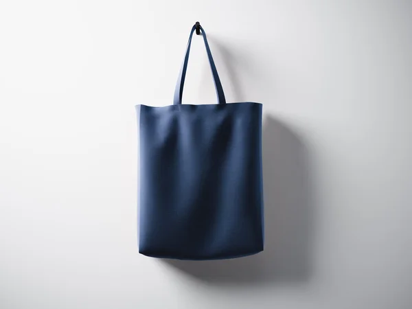 Fénykép kék pamut textil táska lógó központ. Üres, fehér falháttér. Rendkívül részletes textúra. Vízszintes. 3D-renderelés — Stock Fotó