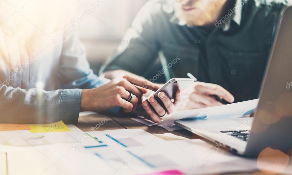 Business meeting partners. Photo young businessmans crew working with new startup project in modern loft. Generic design smartphone holding female hands. Horizontal, film effect