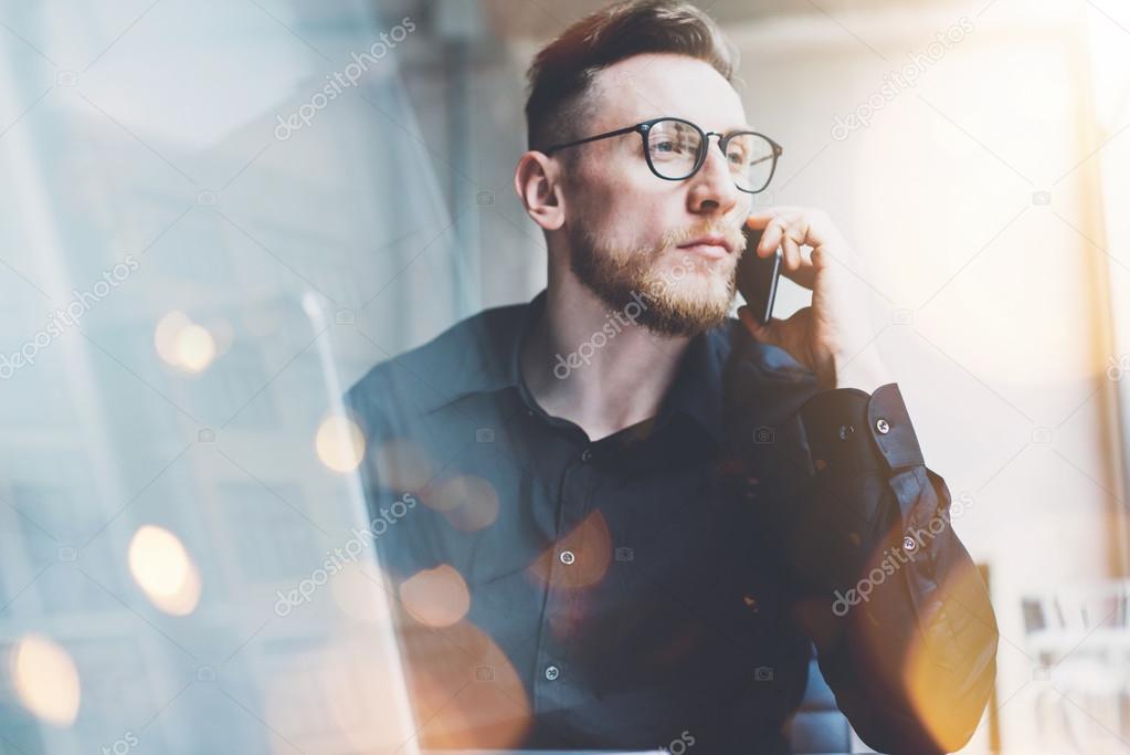 Photo bearded adult businessman working on modern urban cafe. Man wearing black shirt and talking contemporary smartphone. Horizontal, film effect, bokeh. Blurred background