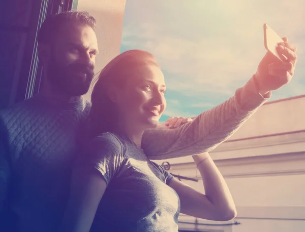 Young couple summer holiday city. Photo woman and bearded man making selfie mobile phone in modern loft. Using contemporary smartphone, smiling. Horizontal, sunlights effect. — Stok fotoğraf