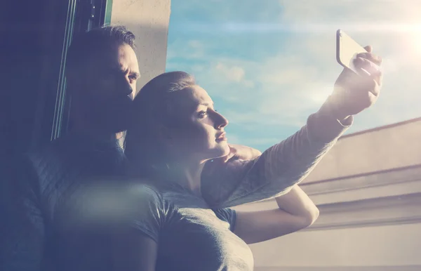 Young couple summer holiday city. Photo woman and bearded man making selfie mobile phone in modern hotel. Using contemporary smartphone. Horizontal, film effect. Sunny sky background — Zdjęcie stockowe