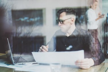 Modern şehir kafede çalışan sakallı yetişkin işadamı. Fotoğraf yalak pencere. Siyah gömlek giyen ve dizüstü bilgisayar arayan, elinde kalem tutan bir adam. Yatay, film efekti, bokeh.