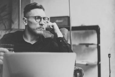 Modern çatı katında çalışan portre sakallı işadamı. Vintage sandalyede oturan, elinde cam su olan bir adam. Çağdaş dizüstü bilgisayar kullanma. Siyah ve beyaz. Yatay, film efekti.