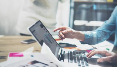 Pazarlama analizi ekibi toplantı konsepti. Modern stüdyoda yeni başlangıç projesi ile çalışan genç işadamı ekibi. Ahşap masa üzerinde genel tasarım dizüstü bilgisayar. Yatay, film efekti