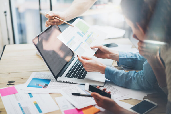 Менеджер по работе с клиентами проекта. Фотография бизнес-менеджеров, работающих с новым стартапом на современном высоком уровне. Анализ отчетов, планов. Ноутбук на деревянном столе, бумаги, документы, статистика. Горизонтальное, размытое
