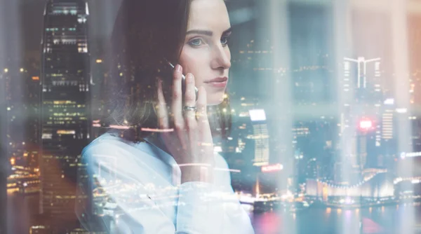 Wanita bisnis foto mengenakan kemeja putih, berbicara smartphone. Buka ruang kantor loteng. Jendela panorama, latar belakang kota malam. Widemockup, kabur, bokeh. Efek film — Stok Foto