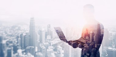 Çift pozlama fotoğraf siyah gömlek ve gözlük giyen sakallı işadamı. Bankacı çağdaş dizüstü ellerini kullanarak, online bankacılık çalışır. Panoramik görünüm modern gökdelen şehir arka plan. Yumuşak ışık