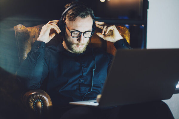 Изображение бородатый человек в очках расслабляющий современный лофт office. Банкир сидит винтажный стул, слушать музыку ноутбук night.
