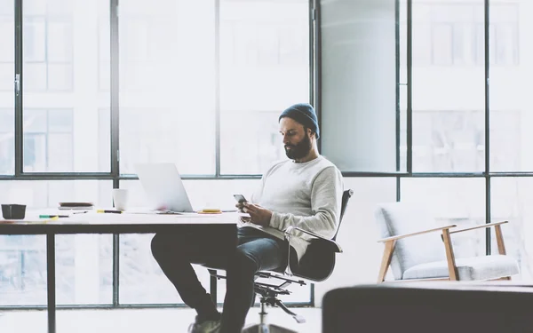 Bärtiger Produktmanager, der an einem modernen Großraumbüro arbeitet. stilvoller Mann SMS-Smartphone. generisches Design Notizbuch Holz Tisch. horizontale Attrappe. Filmeffekt. — Stockfoto