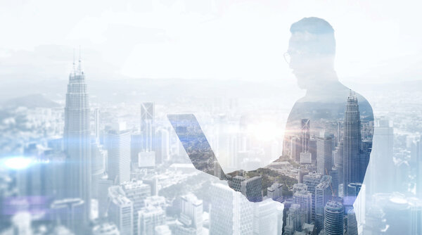 Double exposure photo stylish businessman wearing black shirt and glasses.Banker holding contemporary notebook hands,work online banking.Panoramic view modern skyscraper city background.Soft light