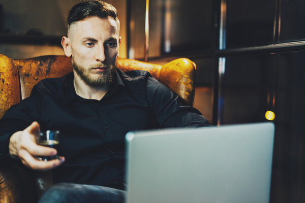 Фото бизнесмен расслабляющий современный лофт-офис после рабочего дня. Мужчина, сидящий ночью в винтажном кресле. Используя современный ноутбук, размытый фон. Мягкий свет, тени. Горизонтальный, эффект пленки
.