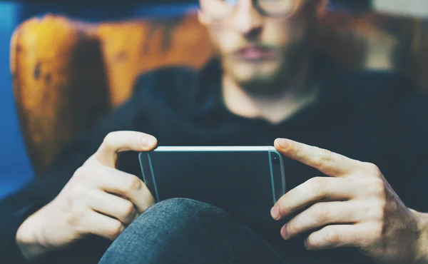 Photo homme d'affaires barbu relaxant bureau loft moderne. Banquier assis dans une chaise vintage, regardant la vidéo. Utilisation d'un smartphone contemporain. Fond flou. Horizontal, effet film . — Photo