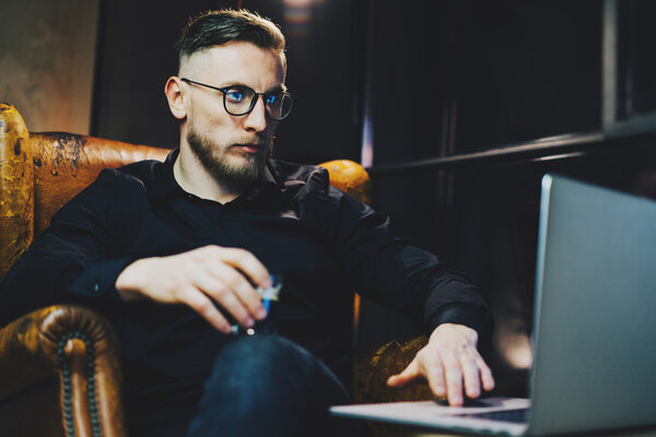 Фото стильный банкир расслабляющий современный лофт-офис после рабочего дня. Мужчина, сидящий ночью в винтажном кресле. Используя современный ноутбук, размытый фон. Мягкий свет, тени. Горизонтальный, эффект пленки
.