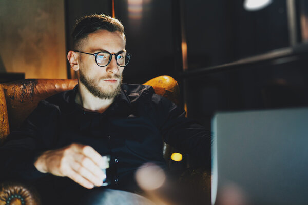 Фото бородатый банкир расслабляющий современный лофт офис после рабочего дня. Мужчина, сидящий ночью в винтажном кресле. Используя современный ноутбук, размытый фон. Мягкий свет, тени. Горизонтальный, эффект пленки
.
