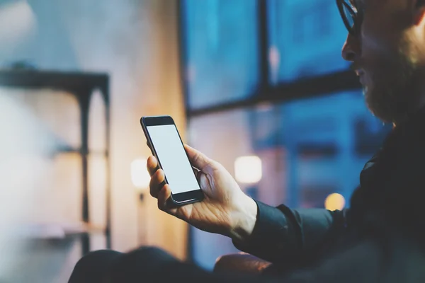 Foto zakenman ontspannend modern Loft kantoor. Man vergadering stoel nacht. Met behulp van hedendaagse smartphone, onscherpe achtergrond. Leeg scherm klaar voor uw bedrijfsinformatie. Horizontaal, filmeffect. — Stockfoto