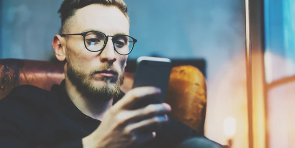 Photo homme d'affaires barbu relaxant bureau loft moderne. Banquier assis dans une chaise vintage, regardant téléphone mobile. Utilisation d'un smartphone contemporain. Fond flou. Large, effet film . — Photo