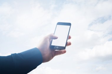 Çift pozlama fotoğraf işadamı modern akıllı telefon eli tutarak, boş beyaz ekran dokunmadan. Arka planı bulutlar, iş bilgileriniz için hazır. Yatay bir maket. Film efekti