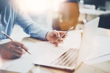 Çalışma süreci fotoğraf. Yeni proje ile ahşap masa çalışma Yöneticisi. Modern dizüstü tablo. Elini tutarak, çağdaş smartphone yazmaya kalem. Yatay. Fişekleri, film etkisi. Arka plan bulanık