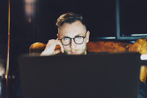 Фото молодой менеджер, работающий в современном лофт-офисе. Мужчина, сидящий ночью в винтажном кресле. Используя современный ноутбук, размытый фон. Мягкий свет, тени. Горизонтальный, эффект пленки
.