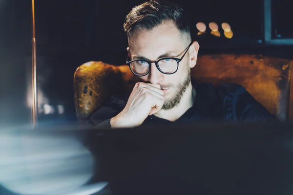 Direttore barbuto che lavora in un moderno ufficio loft. Uomo seduto in sedia vintage di notte, thinkig nuovo progetto startup. Sfondo sfocato. Luce soffusa, ombre. Effetto orizzontale, pellicola . — Foto Stock