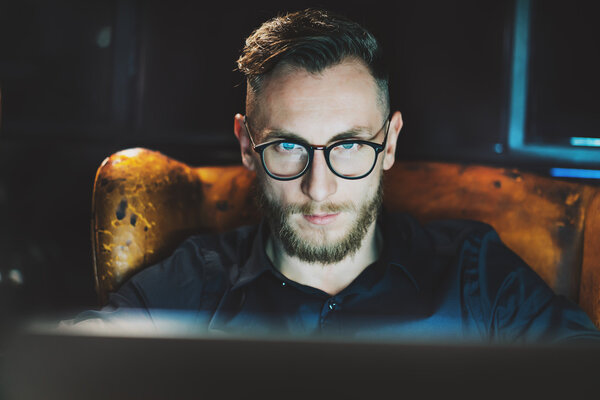 На фото молодой менеджер по работе с клиентами, работающий в современном мансардном офисе. Мужчина, сидящий ночью в винтажном кресле. Используя современный ноутбук, размытый фон. Мягкий свет, тени. Горизонтальный, эффект пленки
.