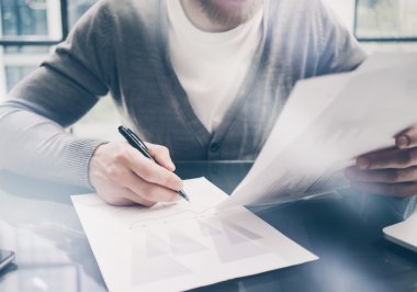 Working process. Account manager working at the wood table with new business project.Holding pen hand, signs document and analyze plans. Horizontal mockup, sunny effect. Blurred, film effect