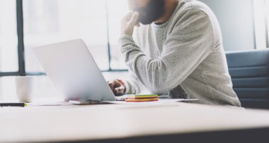 Resim sakallı grafik tasarımcı yeni proje modern loft ile çalışıyor. Ahşap masa üzerinde tefeksyon dizüstü bilgisayar kullanma. Düşünme fikri. Birlikte çalışma dünyası. Bulanık arka plan, film efekti, geniş