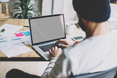 Fotoğraf sakallı grafik tasarımcı yeni proje modern loft ile çalışıyor. Ahşap masa üzerinde tefeksyon dizüstü bilgisayar kullanma. Yaratıcı süreç. Mockup dizüstü yansımaları ekranı. Bulanık arka plan, film efekti, yatay