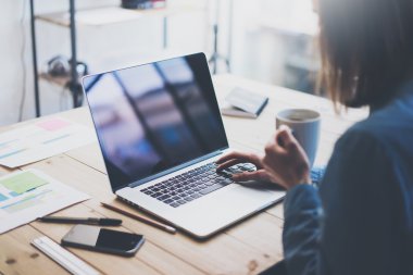 Working process photo.Woman working wood table with new business project.Typing contemporary laptop, reflections screen. Moder smartphone and holding cup of coffee. Horizontal. Film effect,burred