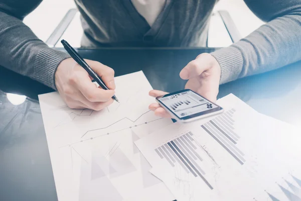 Working process. Account manager working at the table with new business project.Holding modern smartphone hand, statistics screen. Signs document and analyze plans. Horizontal,blurred, film effect — стокове фото