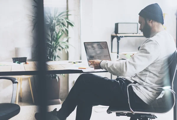 Foto bärtigen Grafik-Manager arbeitet mit neuen Projekt modernen Loft. mit zeitgenössischem Laptop auf Holztisch. kreativer Prozess. Freiberufler. verschwommener Hintergrund, Filmeffekt, horizontal — Stockfoto