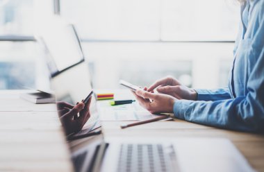Working process photo. Account manager working wood table with new business project. Typing contemporary smartphone screen. Modern notebook reflections screen.Horizontal.Film effect,blurred
