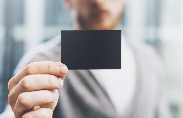 Closeup photo man wearing casual shirt and showing blank black business card. Blurred background. Ready for private information. Horizontal mockup