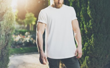 Fotoğraf sakallı kaslı adam giyen beyaz boş t-shirt. Yeşil Park arka plan ve güneş ışığı etkisi. Yatay Mockup