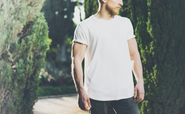 Fotoğraf sakallı kaslı adam giyen beyaz boş t-shirt. Yeşil Park açık arka plan ve güneş ışığı etkisi. Yatay Mockup
