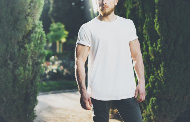Fotoğraf sakallı kaslı adam giyen beyaz boş t-shirt. Green Garden açık arka plan ve güneş ışığı etkisi. Yatay Mockup