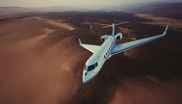 Imagen de White Luxury Generic Design Private Jet Volando en el cielo bajo la superficie de la Tierra. Montañas del Desierto Deshabitadas Fondo. Viajes de negocios. Amplia vista lateral. Efecto de película. Renderizado 3D . — Foto de Stock