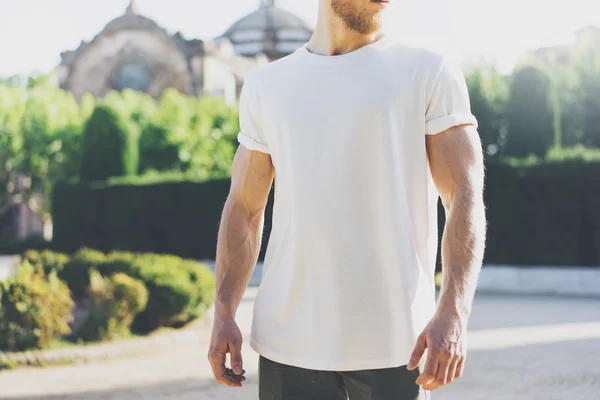 照片胡须肌肉男人穿白色空白 t 恤。在夏天的时候。在日落时的绿色城市花园背景。水平的样机 — 图库照片