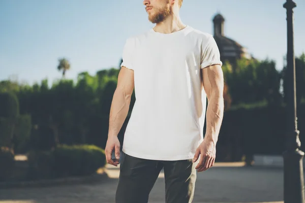 Foto skäggiga muskulös mannen bär vit Blank t-shirt. Green City Garden bakgrund vid solnedgången. Horisontella Mockup — Stockfoto