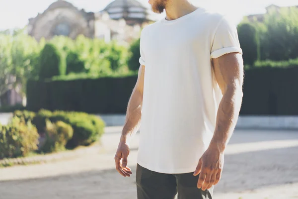 Immagine uomo muscoloso barbuto con indosso bianco Blank t-shirt. Green City Garden Sfondo al tramonto. Mockup orizzontale — Foto Stock