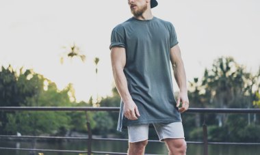 Fotoğraf Sakallı Kaslı Adam Gri Boş t-shirt ve şort yaz saati giyiyor. Green City Garden Lake Arka Plan, bulanık. Yatay Mockup