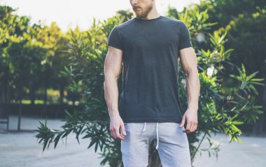 Fotoğraf Sakallı Kaslı Adam Yaz tatilinde Siyah Boş t-shirt ve şort giyiyor. Göl kenarında dinlendirici bir zaman. Green City Garden Park Sunset Arka Plan. Ön görüş. Yatay Mockup.