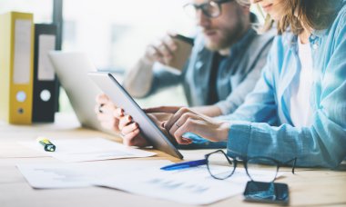 İş arkadaşları yaratıcı stüdyoda çalışır. Üretim yöneticileri ekibi yeni proje çalışıyor. Genç iş ekibi tartışma başlangıç. Ahşap masa üzerinde dizüstü bilgisayar, dijital tablet kullanarak. Bulanık, film efekti. Yatay.