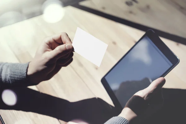 空白の白い名刺を示すフォトマン、手を握る現代のデジタルタブレット.Woodテーブルぼやけた背景.モックアップ準備ができて個人情報.太陽光反射画面ガジェット.水平モックアップ. — ストック写真