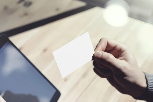 Close-up man toont lege witte visitekaartje, holding hand moderne digitale Tablet. hout tabel wazig achtergrond. mockup klaar prive-informatie. zonlicht reflecties scherm gadget. horizontaal mock up. — Stockfoto