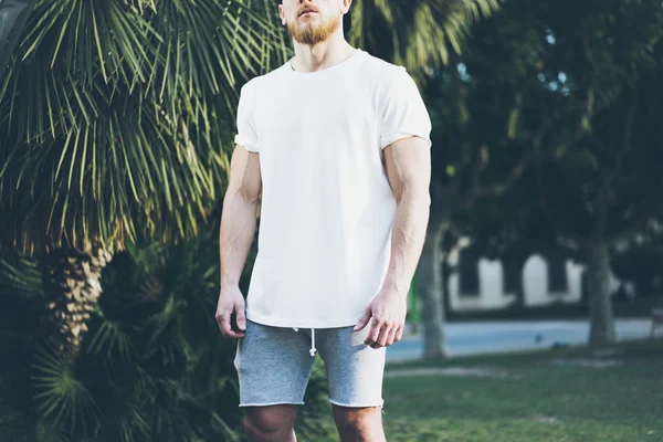 照片胡子肌肉男子穿着白色空白T恤和短裤在夏季时间。绿城花园背景，模糊。水平模拟 — 图库照片