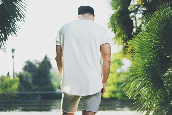 Foto Homem Muscular Barbudo Vestindo t-shirt branca em branco e shorts no verão. Green City Garden Park Fundo. Vista traseira. Mockup horizontal — Fotografia de Stock