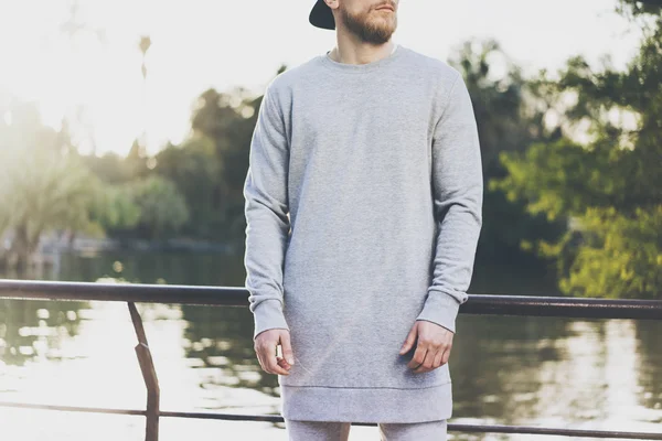 Foto Bearded muskulös man bär grå blank lång sött i sommarsemester. Avkopplande tid nära sjön. Green City Garden Park Sunset bakgrund. vy framifrån. Horisontellt utkast — Stockfoto