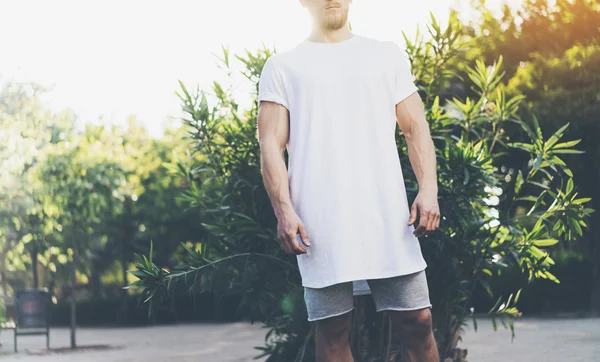 Foto Bearded Muscular Man Indossare bianco Blank t-shirt e pantaloncini in vacanza ora legale. Green City Garden Park sfondo. Vista frontale. Mockup orizzontale — Foto Stock