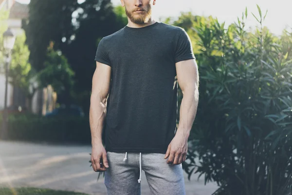 Immagine Bearded Muscular Man Indossare nero T-shirt vuota e pantaloncini durante le vacanze estive. Green City Garden Park sfondo. Vista frontale. Mockup orizzontale . — Foto Stock